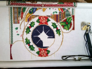 Why Cross Stitch demo image: a work in progress on its stand. Celtic winter motifs. A pair of snips hangs via lanyard from a magnetic needle minder. 