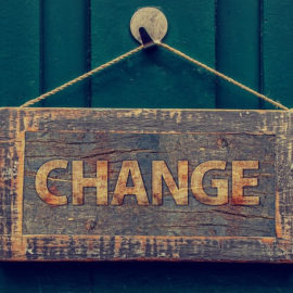 A wooden sign hangs on a painted wooden wall. It says "Change."