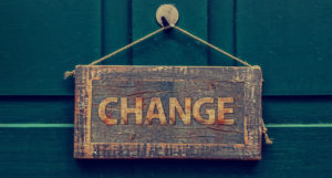 Change is good: In this image, a wooden sign hangs on a painted wooden wall. It says "Change."