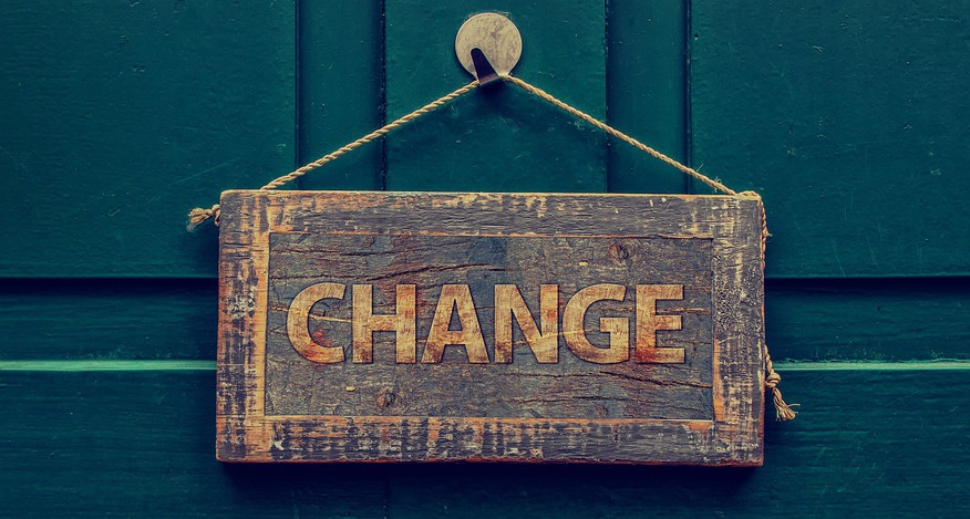 A wooden sign hangs on a painted wooden wall. It says "Change."