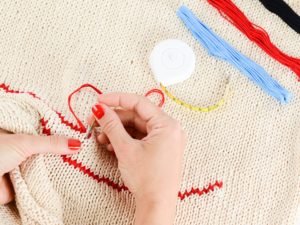 Dry hands? Not here! In this image, a pair of lovely looking hands is stitching red embroidery floss into a sweater. From Grimalkin Crossing.