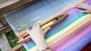 non-dry hands weaving a rainbow on a traditional loom. From Grimalkin Crossing