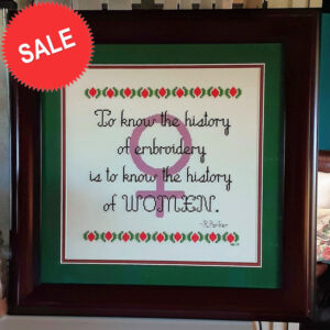 For Grimalkin Crossing's Women's History Month sale. Photo of a tastefully framed finish of History Lesson. Legend says "To know the history of embroidery is to know the history of women." There's a symbol of Venus in the background. This design is on sale through 03/31/23.